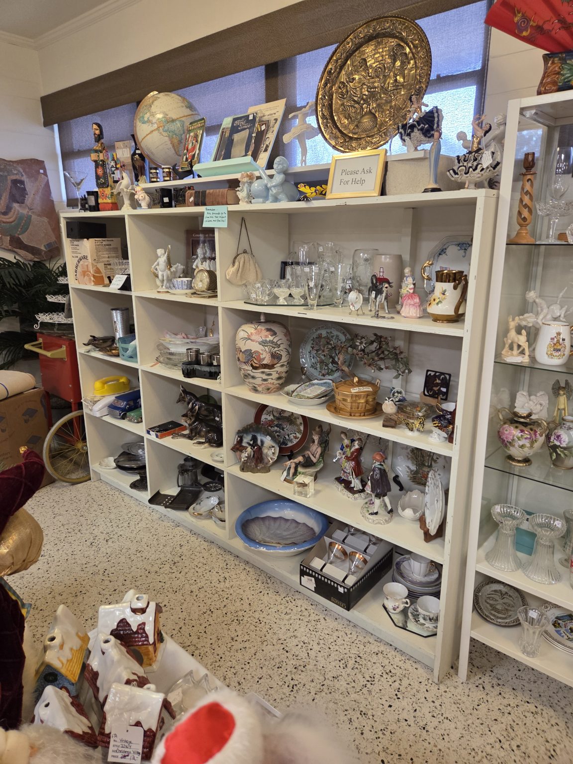 A curated shelf of donated fine china, crystal, and collectibles inside the Winter Park Benefit Shop.